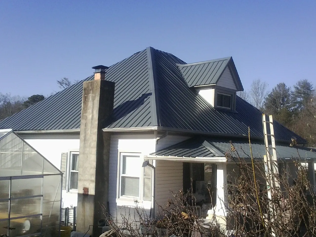 Dark blue standing seam metal roof on a white farmhouse with dormer — Slate & Tile Roof Repair by Roofing Brothers in Oakland Mills