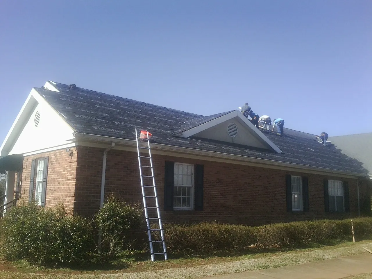 Crew tearing shingles off a brick ranch roof with a ladder set — Metal Roof Repair work by our crew in Oakland Mills
