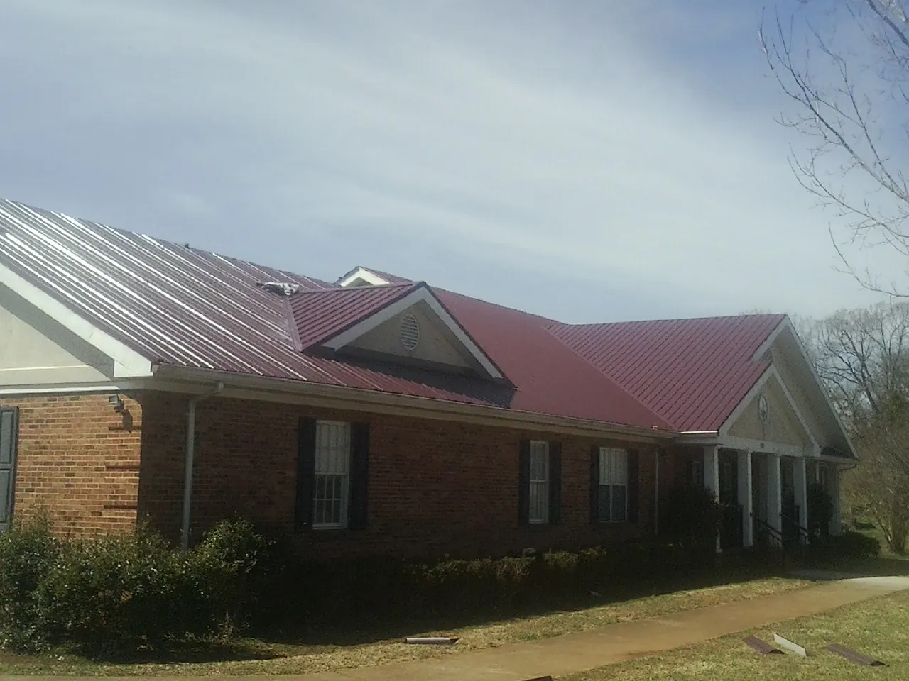 Red metal roof with gabled entries on a long brick building, from a Hail Damage Roof Repair job in Oakland Mills