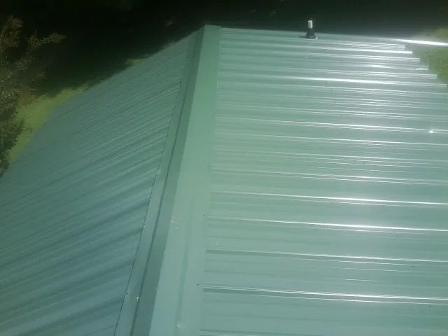New green metal panels meeting at the ridge of a roof — Flat Roof Repair work by our crew in Oakland Mills