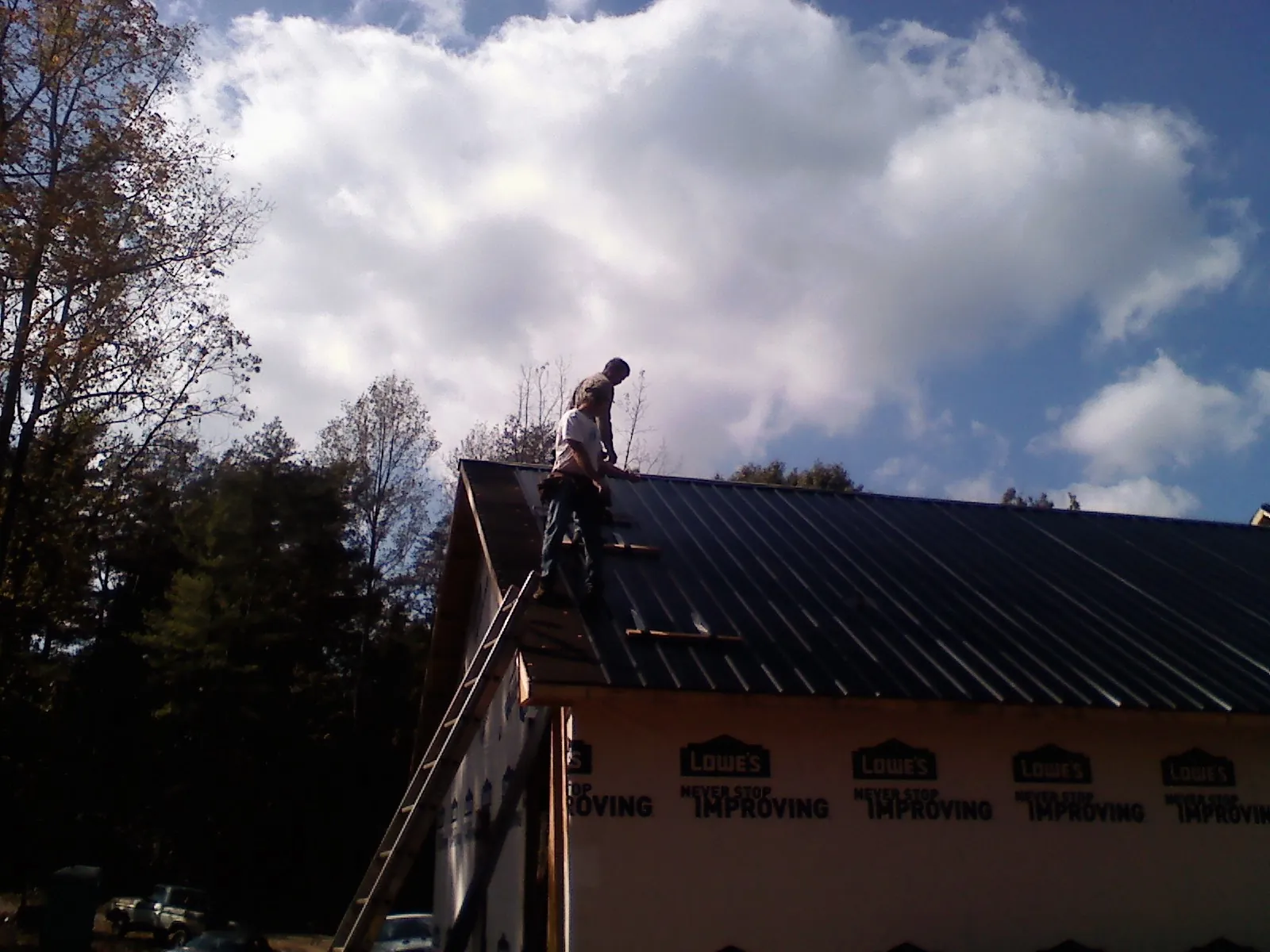 Roofer fastening dark metal panels high against a cloudy sky, from a Roof Inspection job in Oakland Mills