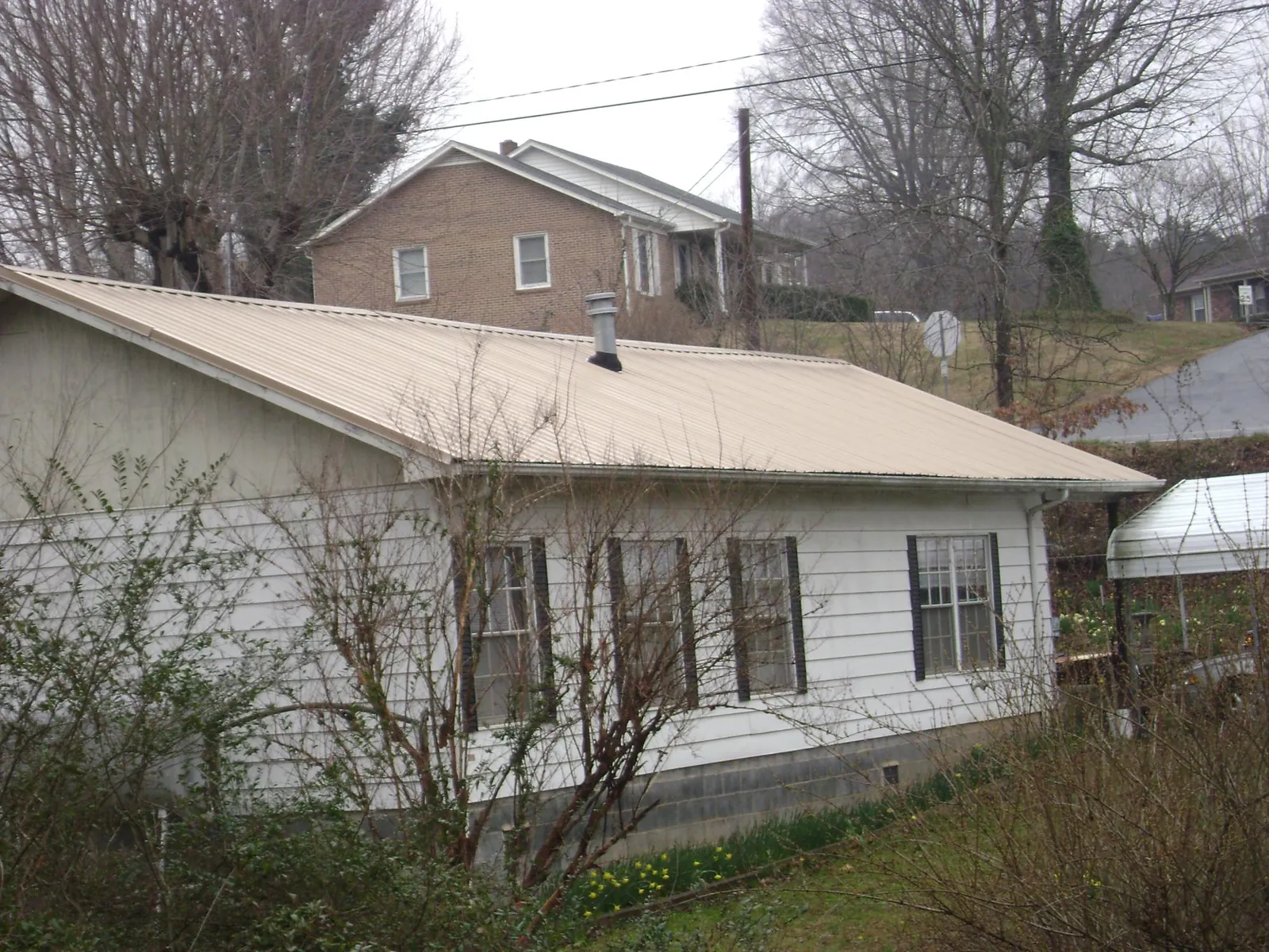 Tan metal roof on a white sided house set into a hillside — Commercial Roofing by Roofing Brothers in Oakland Mills
